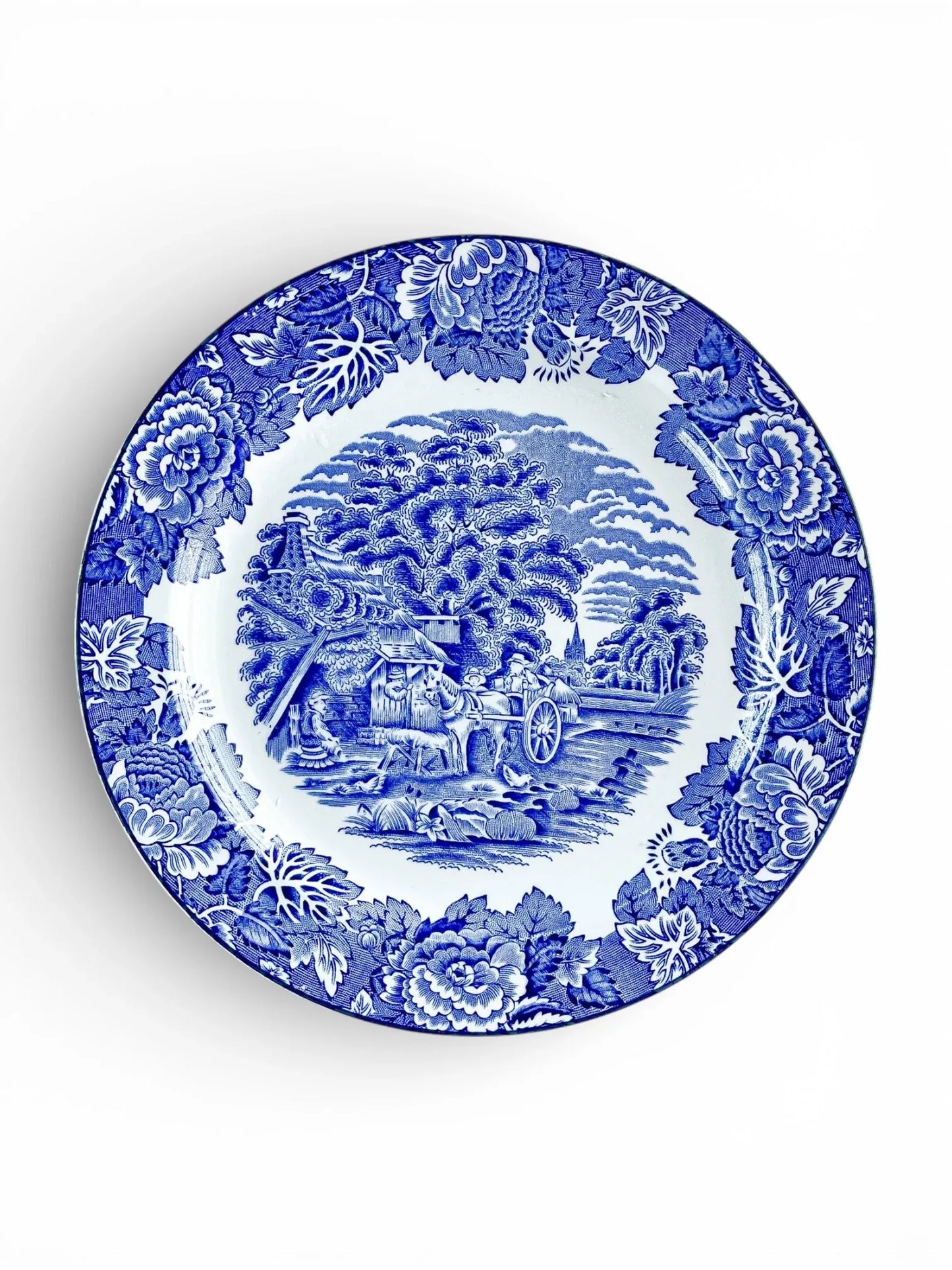 Blue and white vintage ceramic plate with floral border and pastoral countryside scene