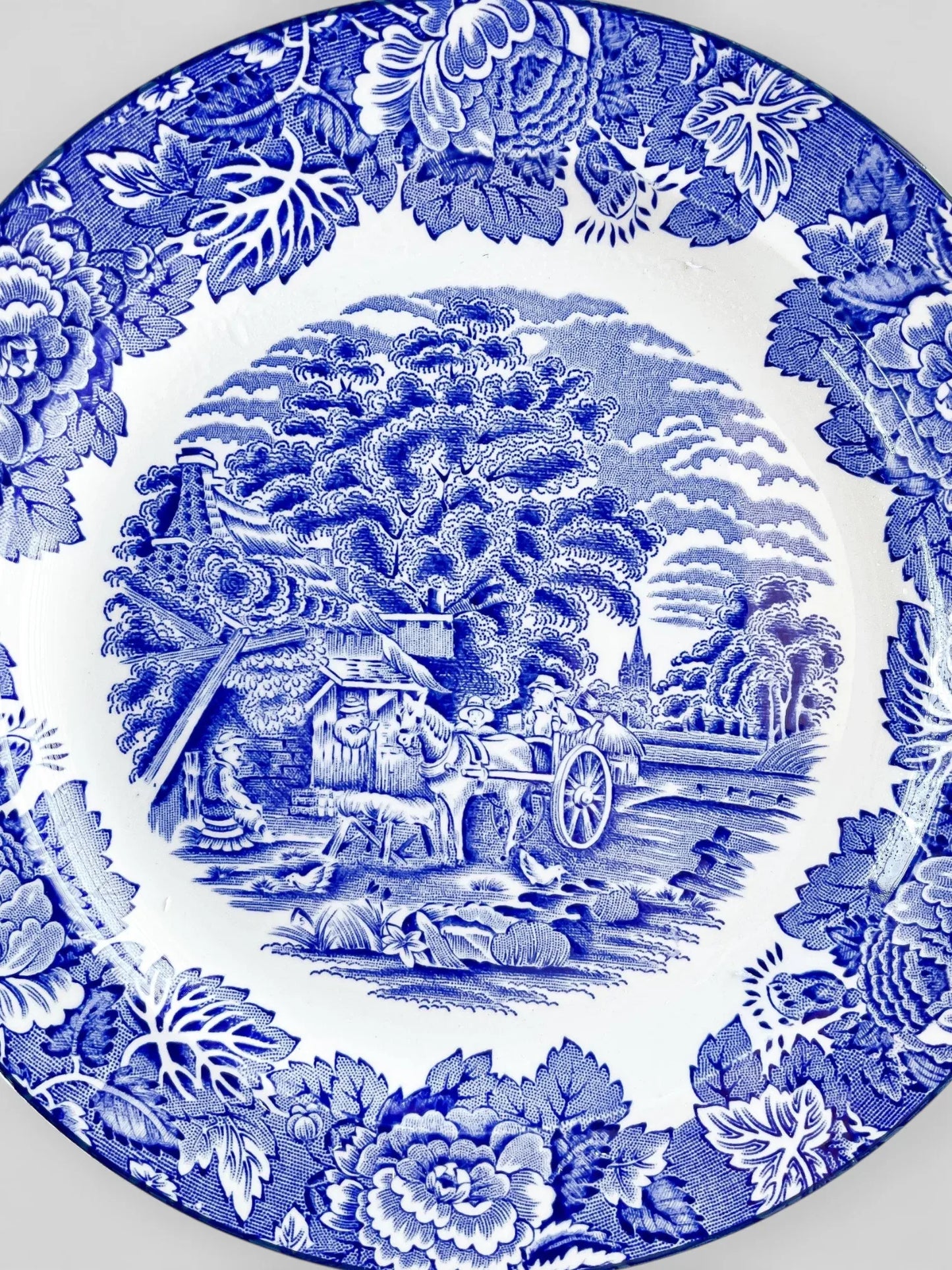 Blue and white vintage porcelain plate with floral border and pastoral countryside scene