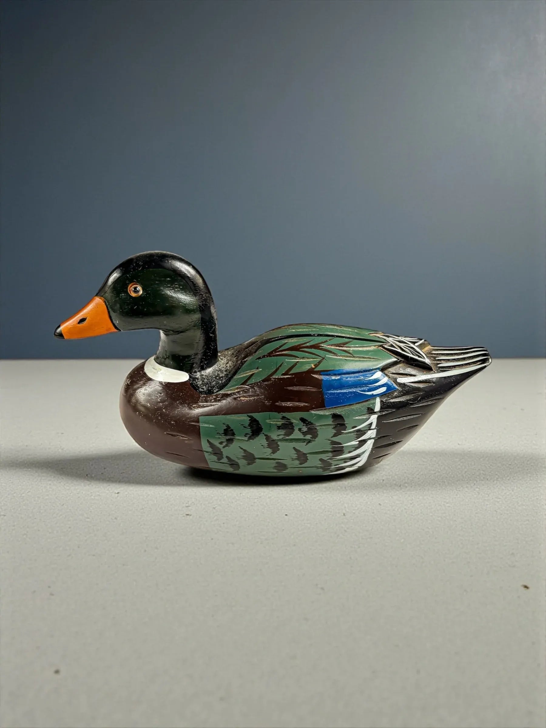 Hand-painted wooden duck decoy with green, brown, blue, and orange details on gray surface