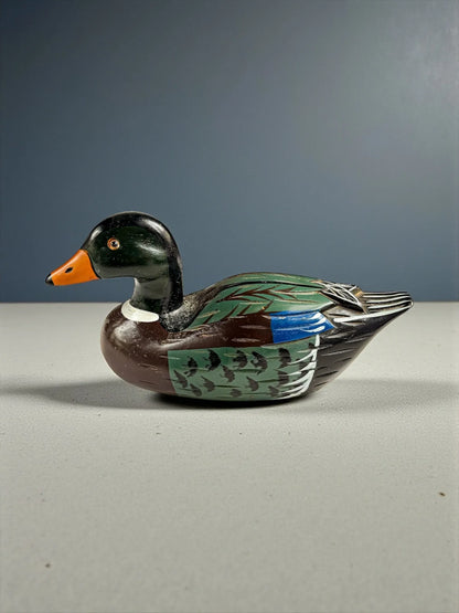 Hand-painted wooden duck decoy with green, brown, blue, and orange details on gray surface