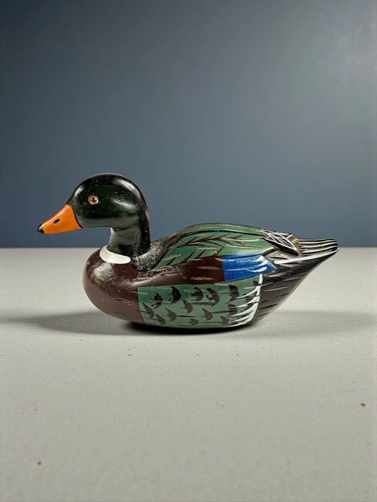 Hand-painted wooden duck decoy with green, brown, blue, and orange details on gray surface