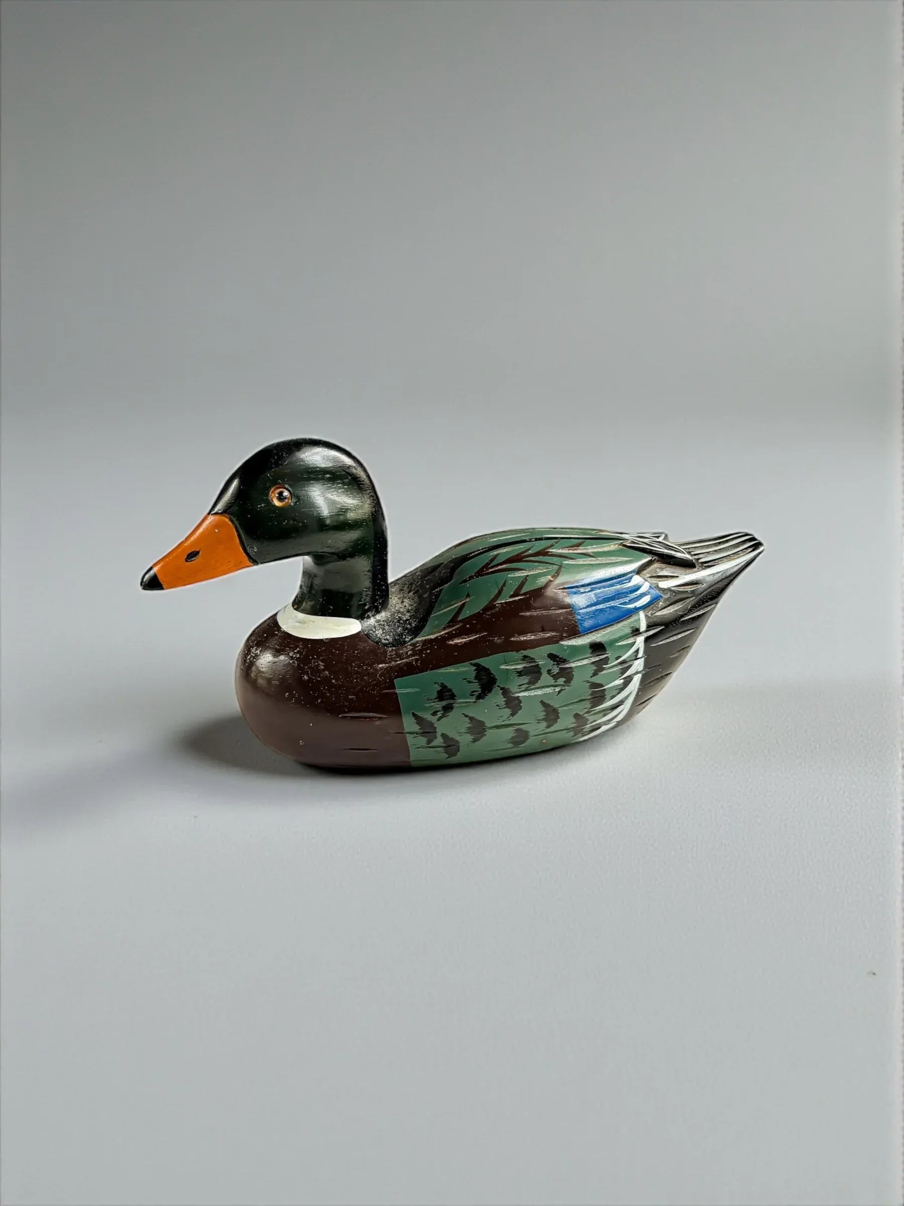 Hand-painted wooden duck decoy with green, brown, orange, and blue colors on gray background
